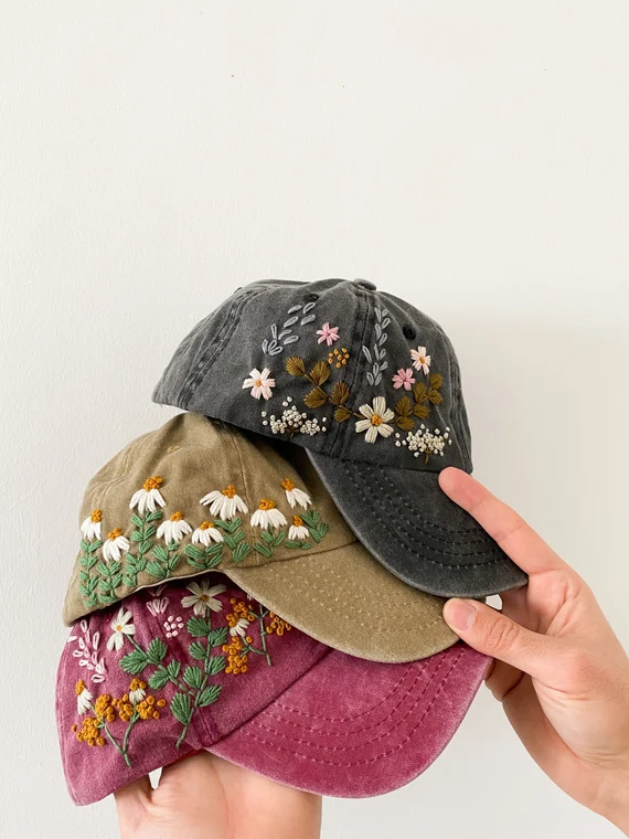 Hand holding three embroidered floral caps