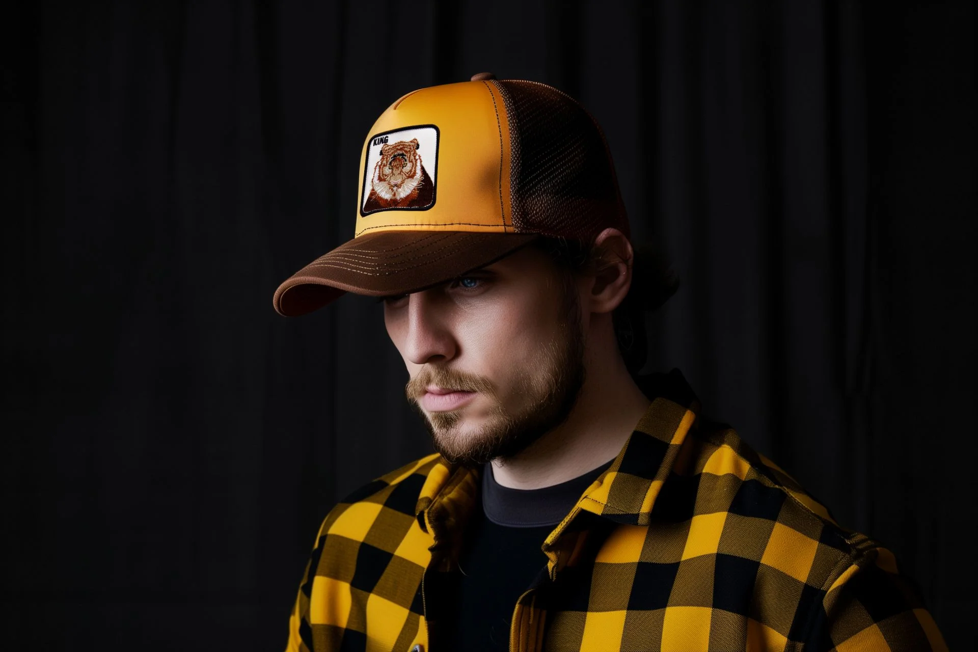 Uomo con un cappello da camionista giallo e marrone con una toppa a forma di orso