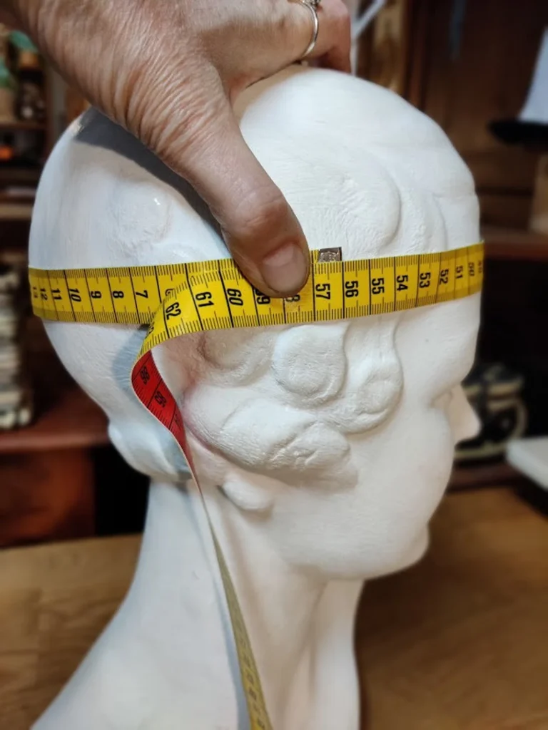 Hand measuring a mannequins head with a tape