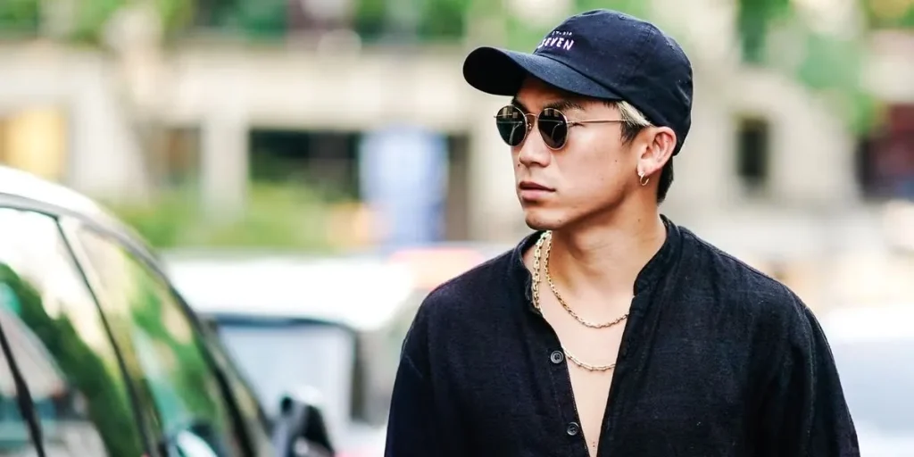 Hombre con gafas de sol y gorra negra, camisa oscura y cadenas