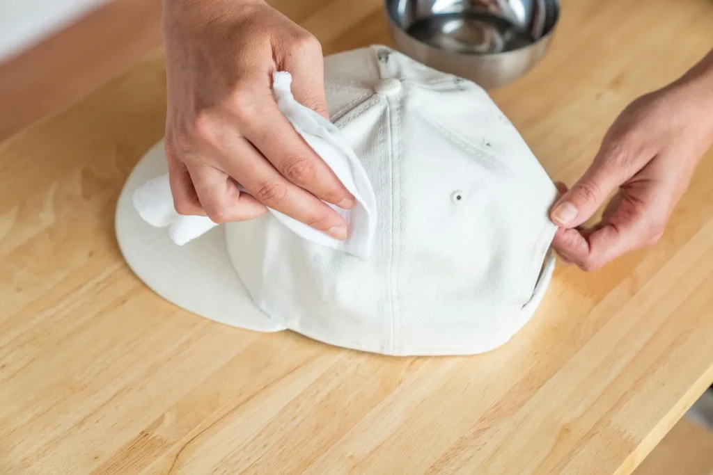 Hands spot cleaning a white baseball cap with a cloth