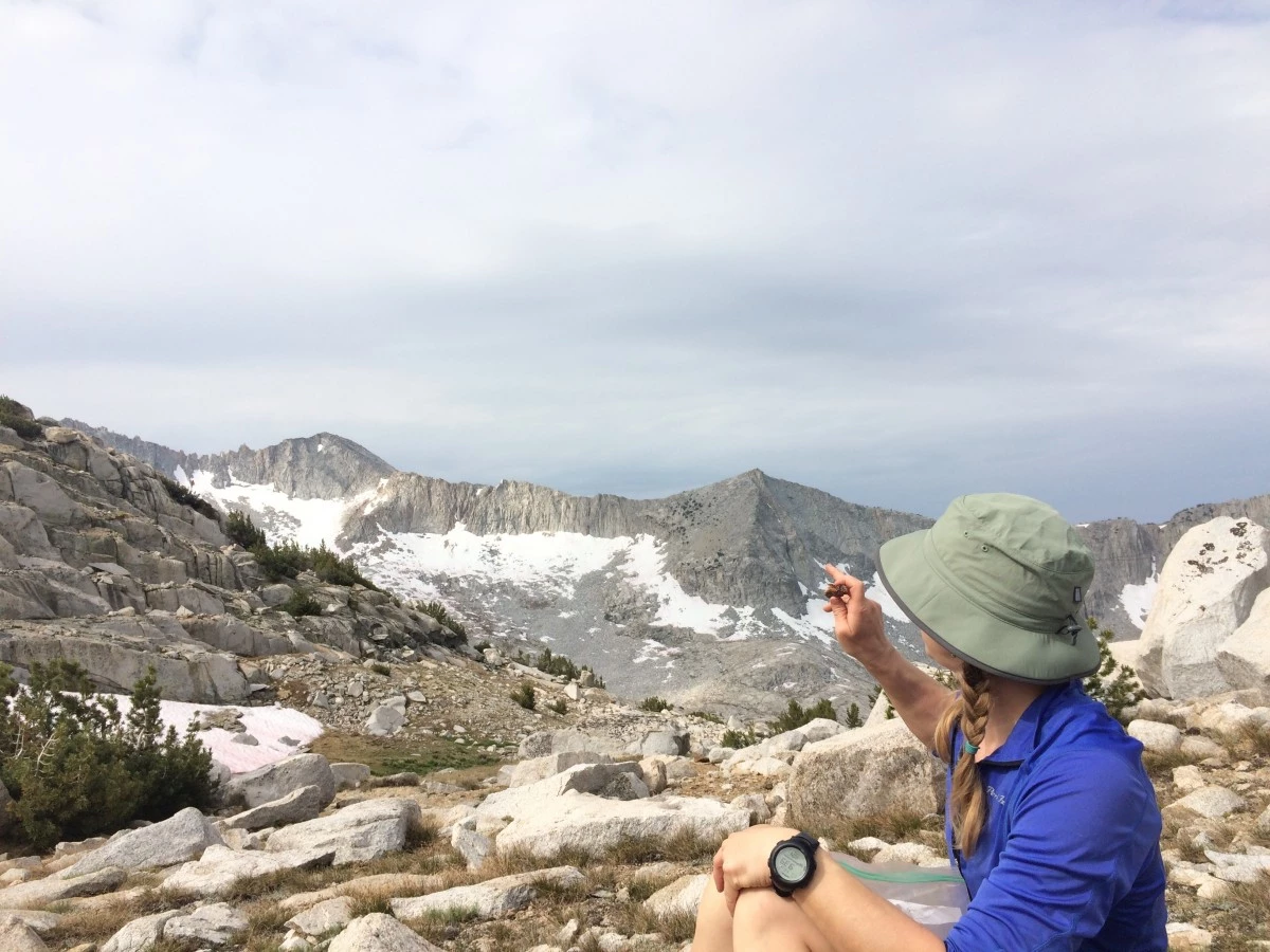 Hiker in green hat points at snowy mountains