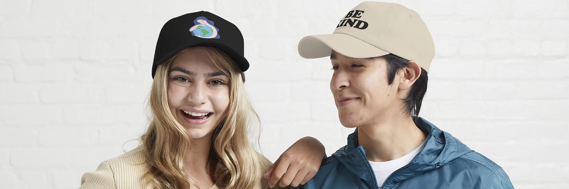 Pareja sonriente con gorras con temática BE KIND y la tierra Pareja sonriente con gorras con temática BE KIND y la tierra