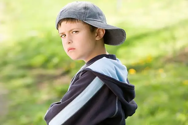Niño joven con gorra gris al aire libre con expresión seria Niño joven con gorra gris al aire libre con expresión seria