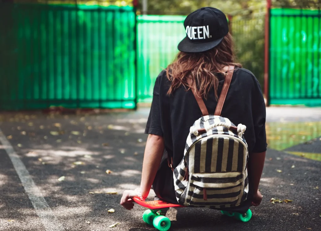 Girl on a skateboard striped bag and caps backwards outdoors
