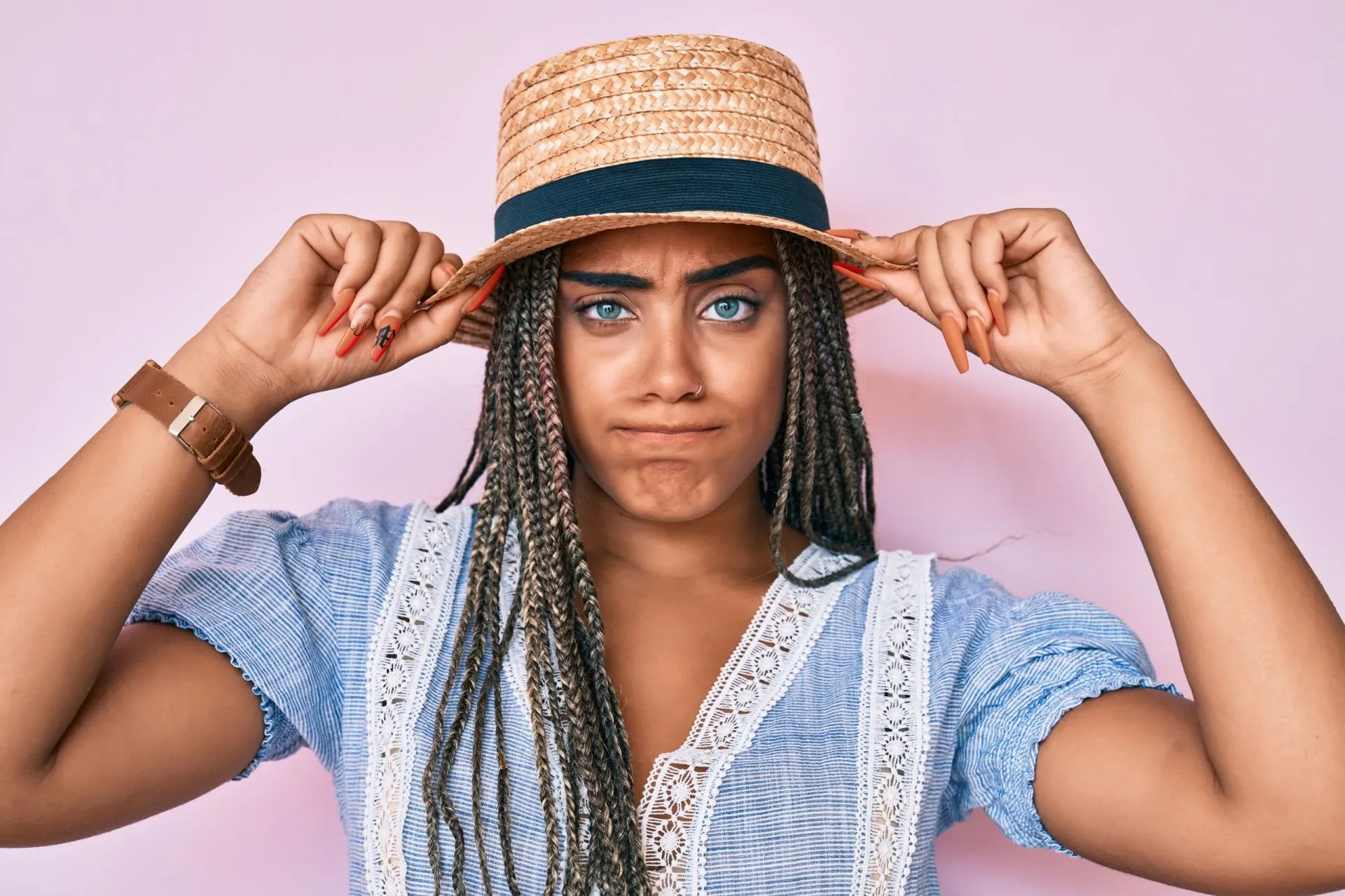Donna scettica aggiusta cappello di paglia sfondo rosa pastello