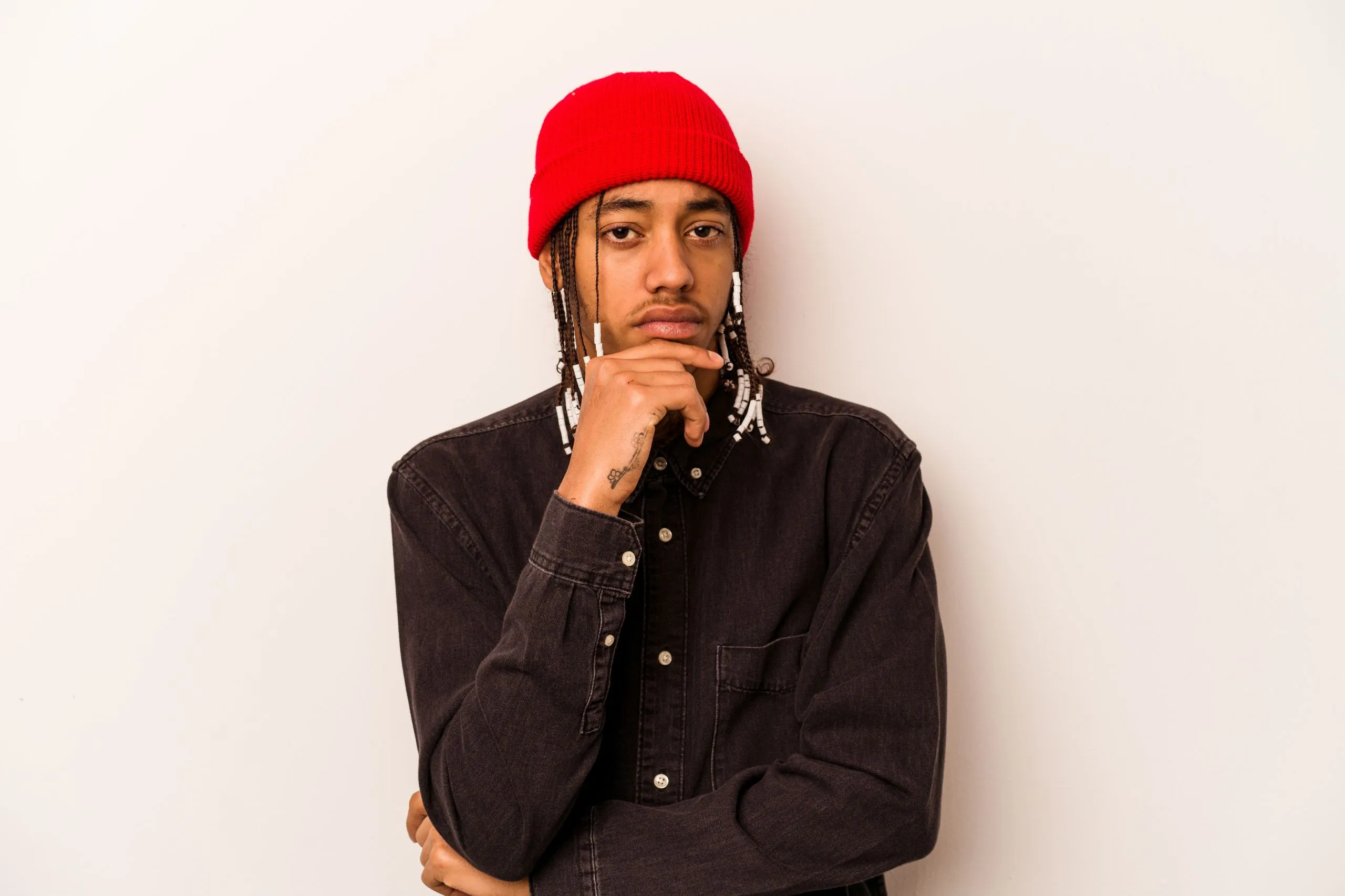Thoughtful man in red beanie rests chin on hand plain backdrop