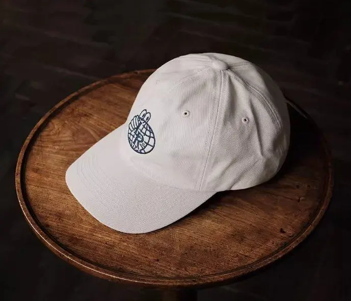 Gorra de papá blanca con bordado de globo terráqueo sobre mesa de madera Gorra de papá blanca con bordado de globo terráqueo sobre mesa de madera