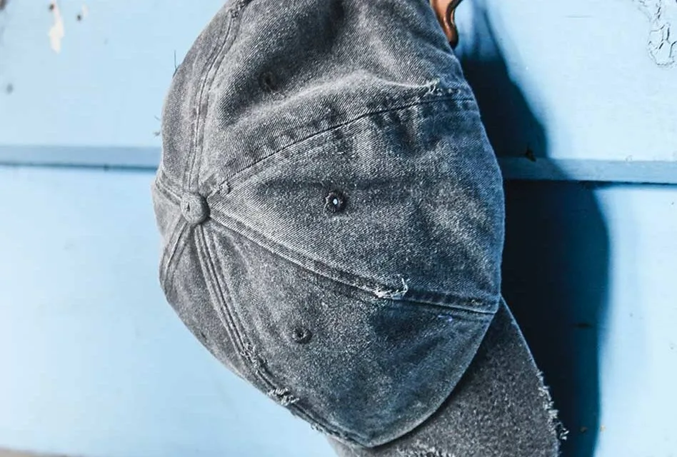 Parte trasera de gorra desgastada Gorra gris con tela deshilachada sobre una superficie azul Parte trasera de gorra desgastada Gorra gris con tela deshilachada sobre una superficie azul