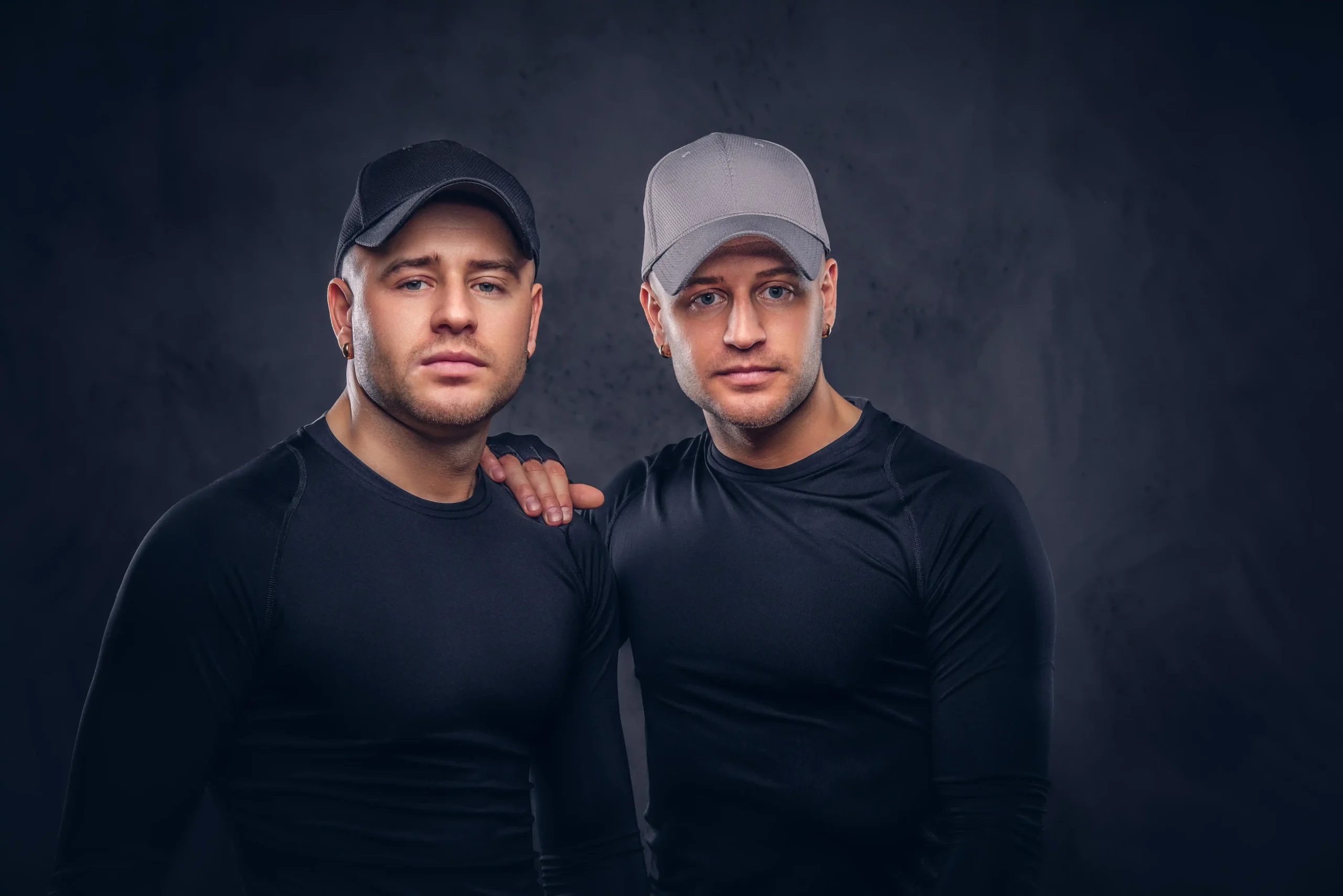 close up portrait two handsome young male dressed black sportswear baseball cap dark background