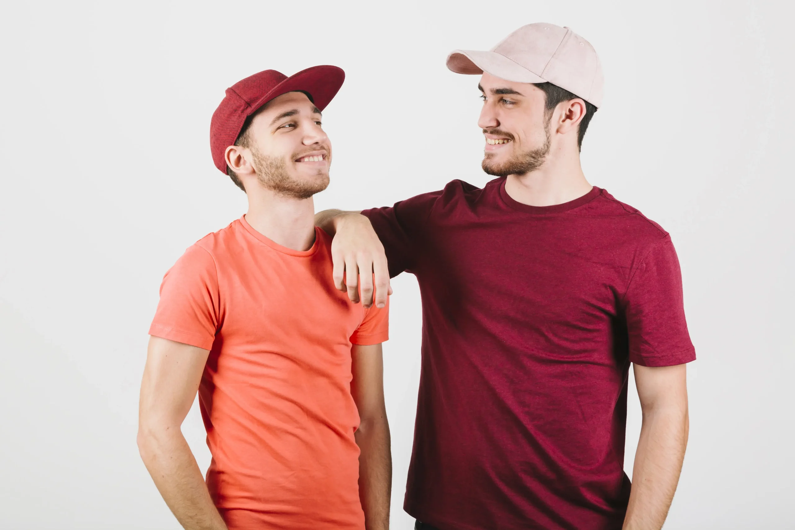 Pareja gay feliz de pie cerca de gorras Pareja gay feliz de pie cerca de gorras