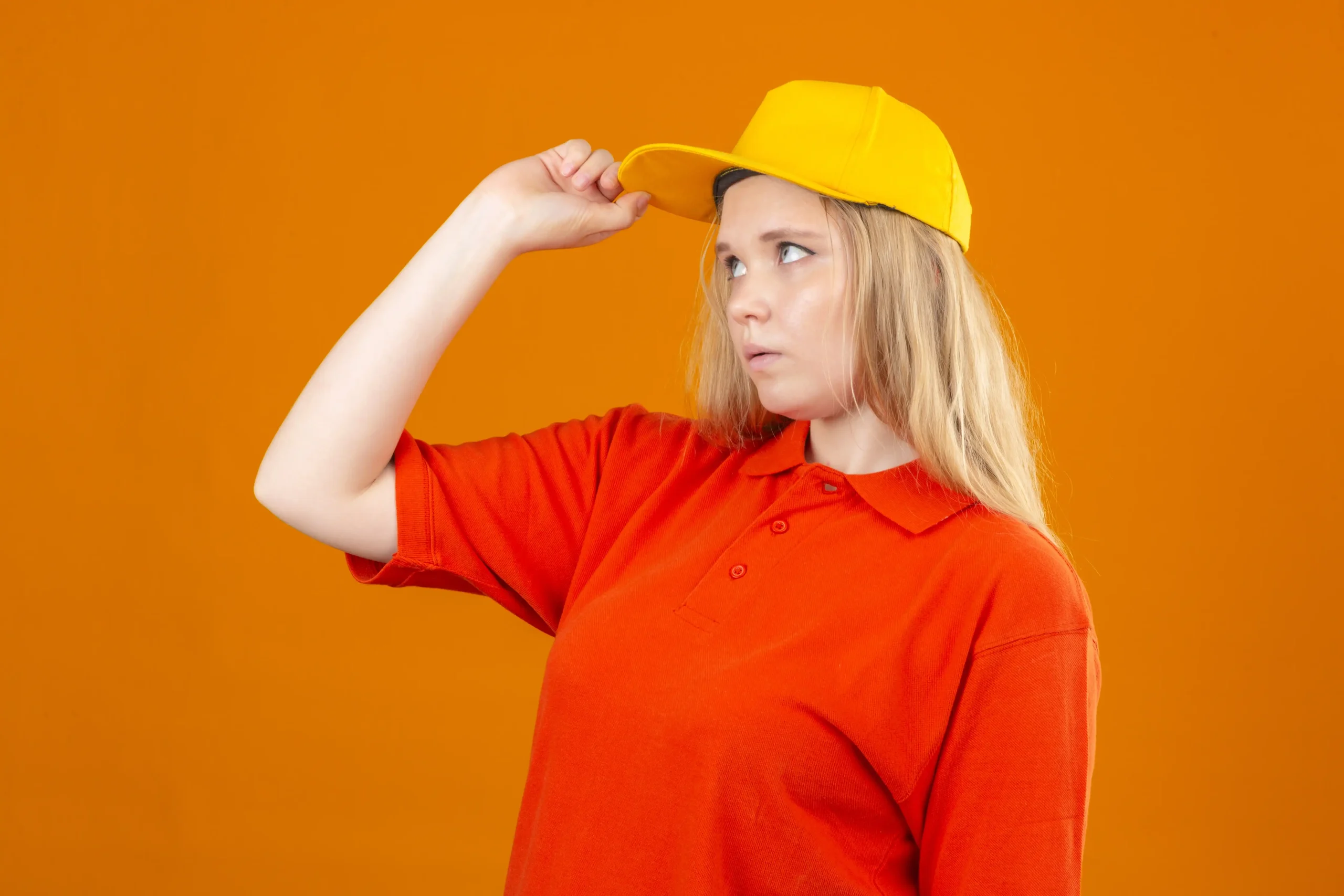 Mujer pensativa con polo rojo y gorra amarilla Mujer pensativa con polo rojo y gorra amarilla