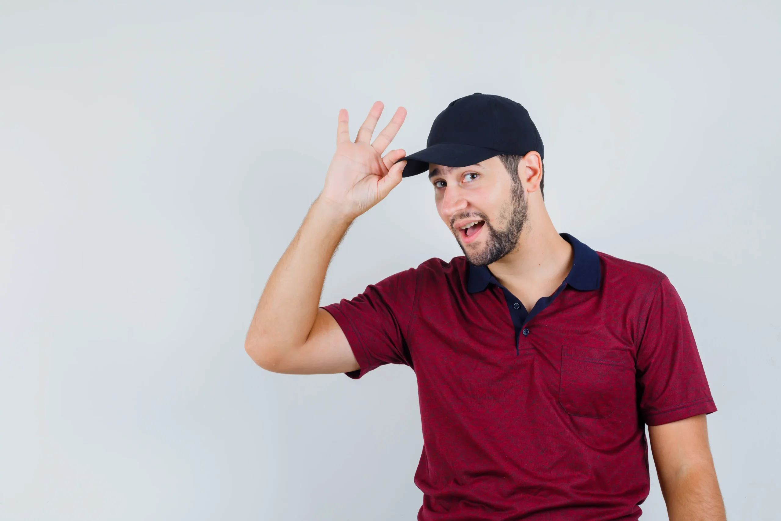 young male holding his cap while looking camera red t shirt black cap looking jolly front view