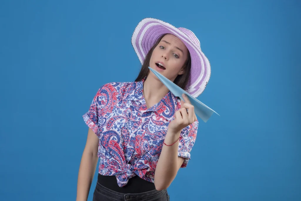 young traveler woman summer hat holding paper airplane playful happy standing blue background