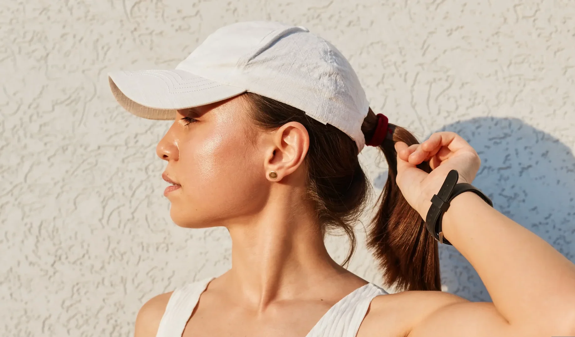 giovane donna caucasica che indossa abiti sportivi con berretto con visiera in piedi vicino al muro all'aperto tenendo la mano