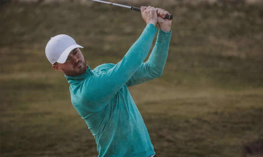 A golfer wearing a white cap swings his club