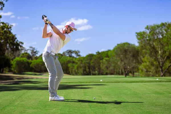A male golfer with a pink cap takes a swing