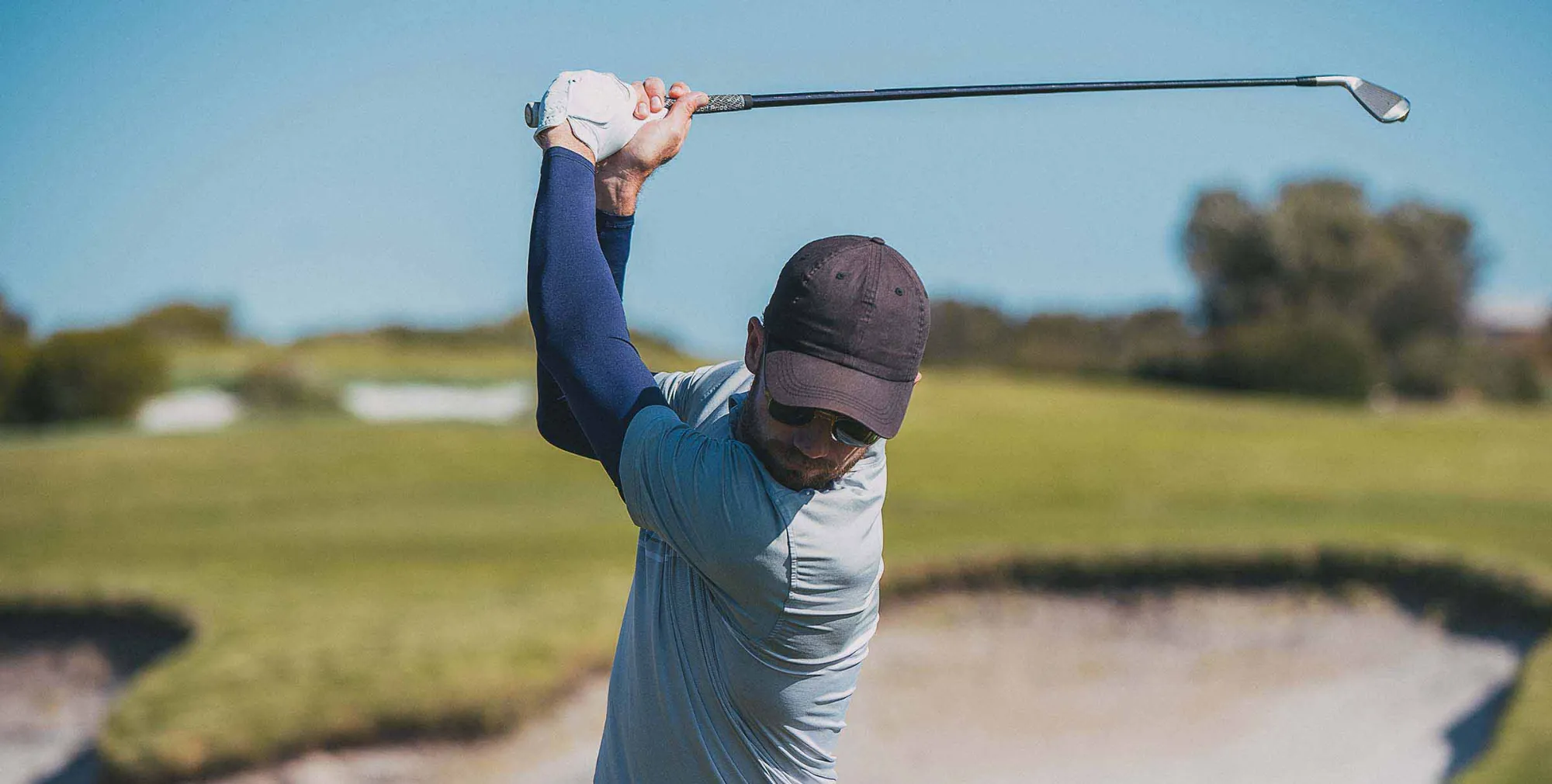 A man in a dark cap and sunglasses swings a club A man in a dark cap and sunglasses swings a club