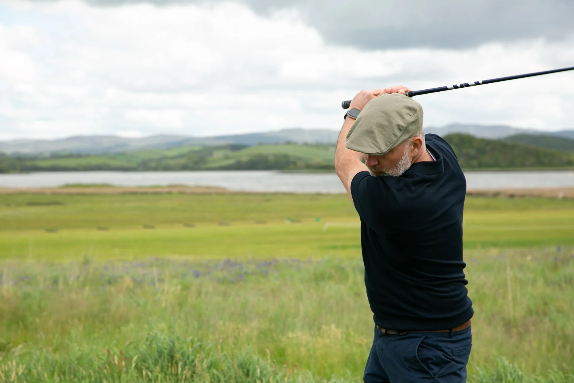 A man in a flat cap swings a golf club A man in a flat cap swings a golf club