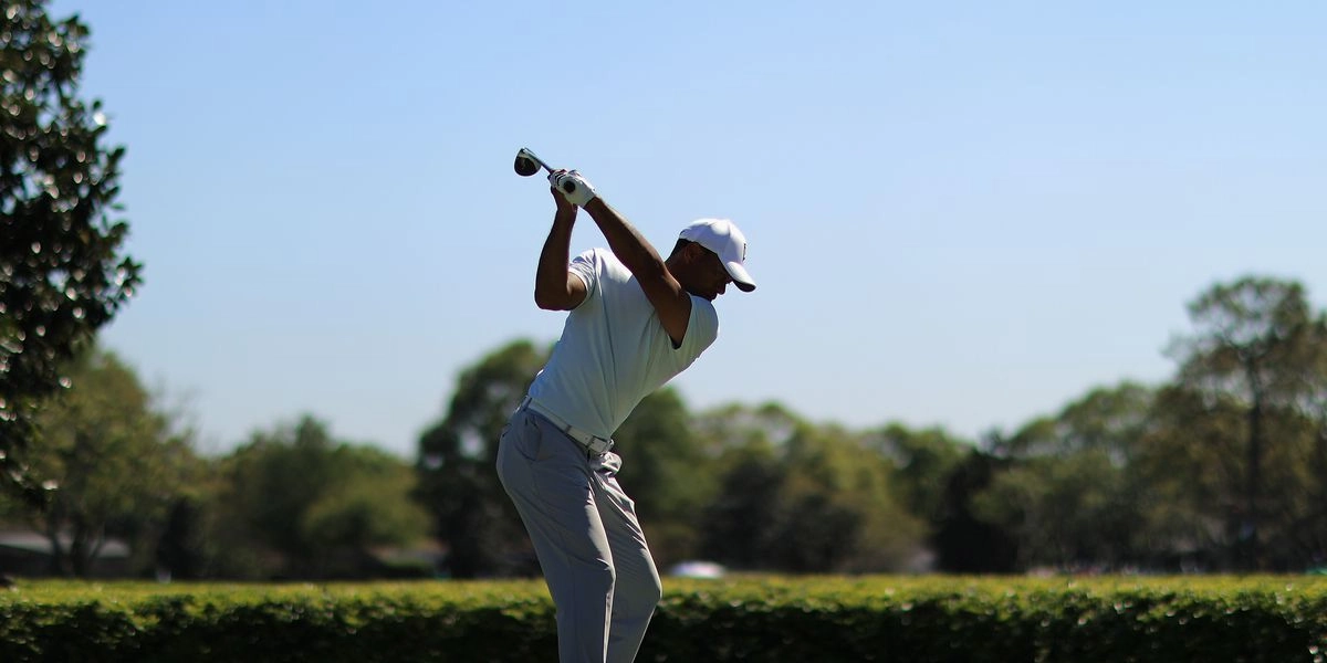 A golfer in a white cap mid swing